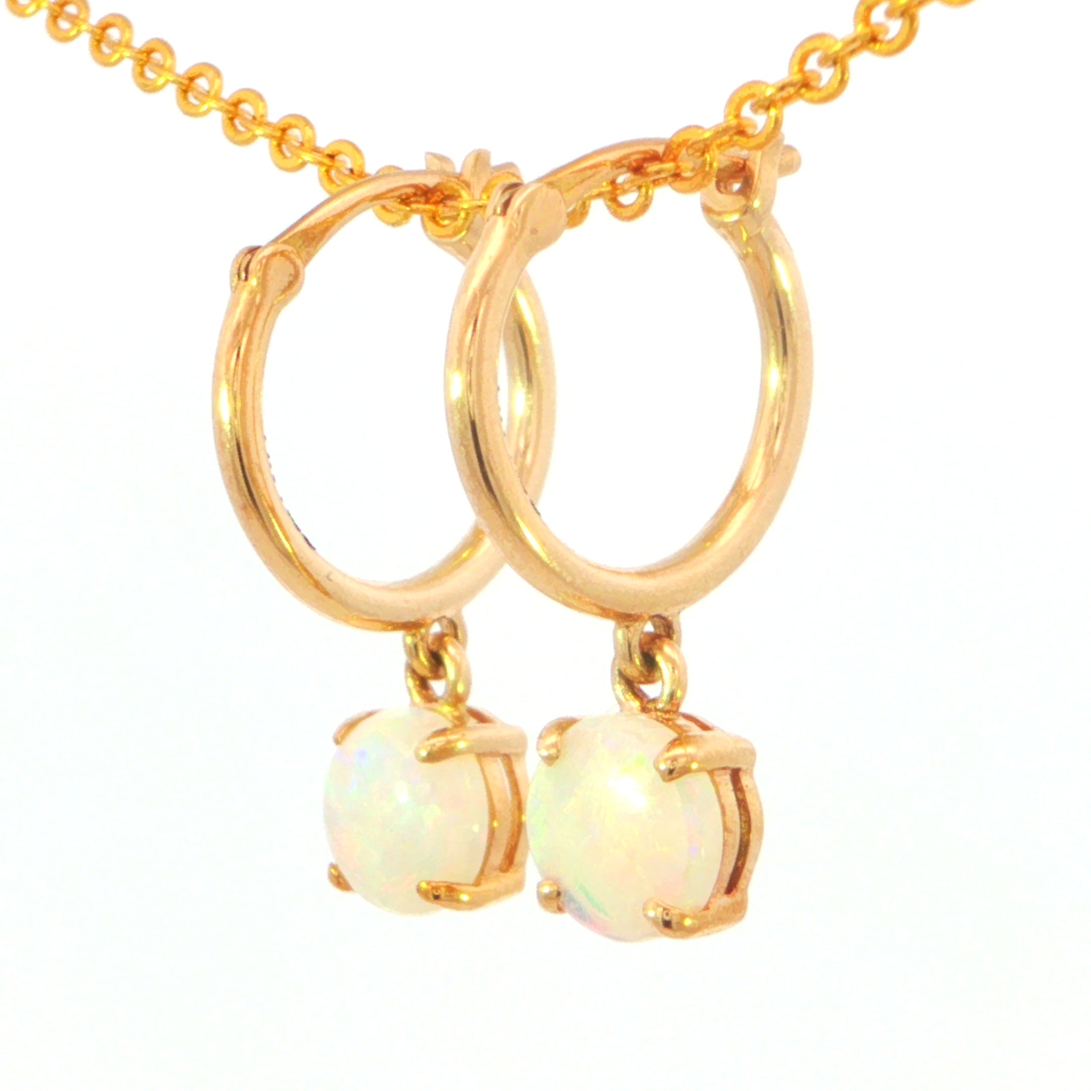 Gold hoop earrings with dangling round iridescent opal-like stones, shown on a gold chain against a white background.