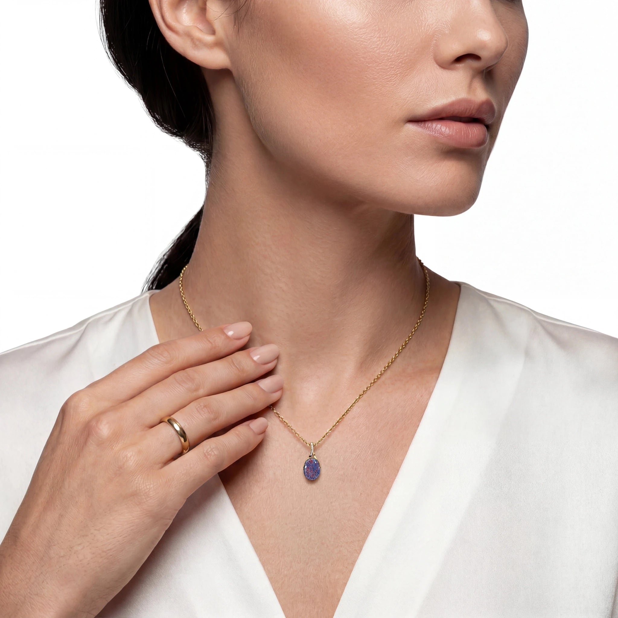 Woman wearing a gold necklace with a multicolour opal pendant on a white background