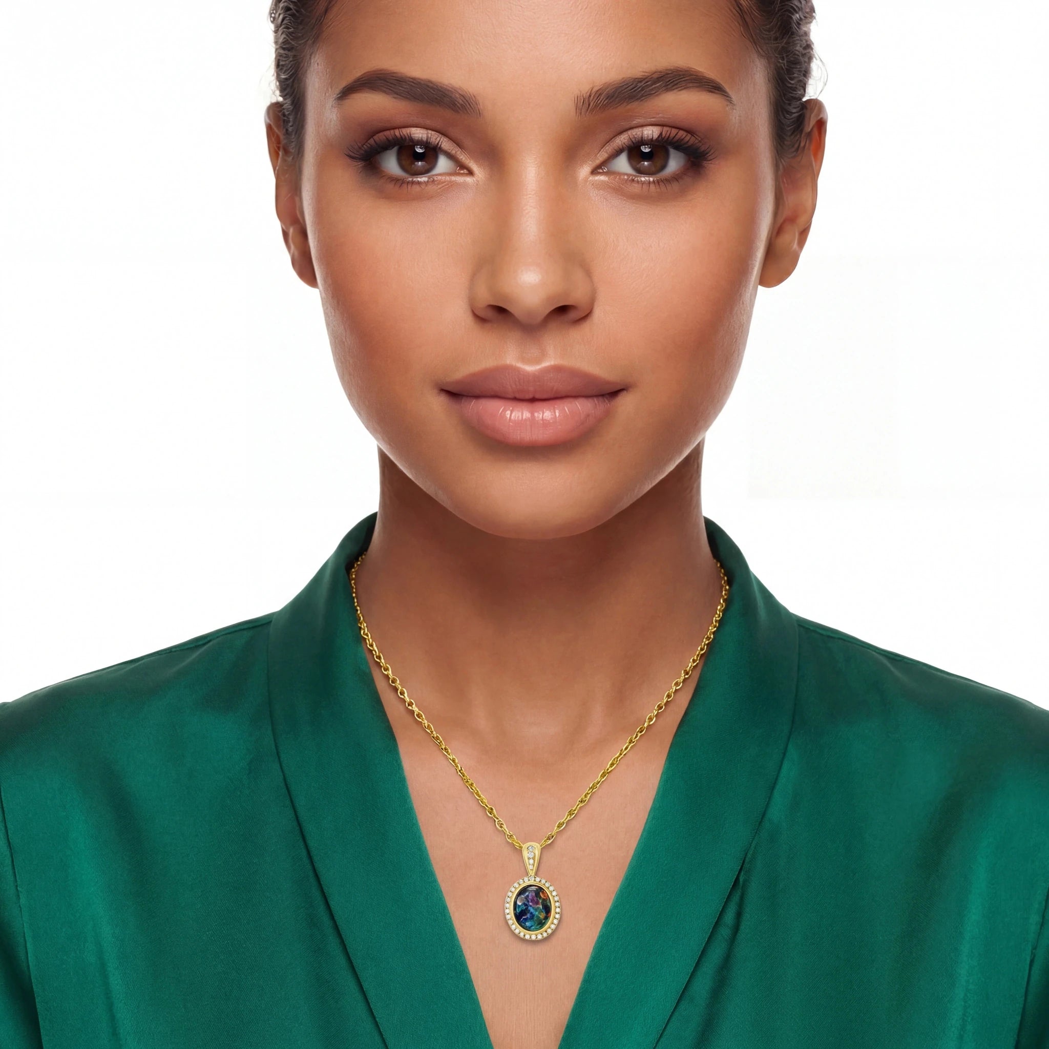 A close-up of a woman wearing a gold chain necklace with an oval pendant featuring a dark blue center and a halo of small clear stones, paired with a green satin top against a white background.