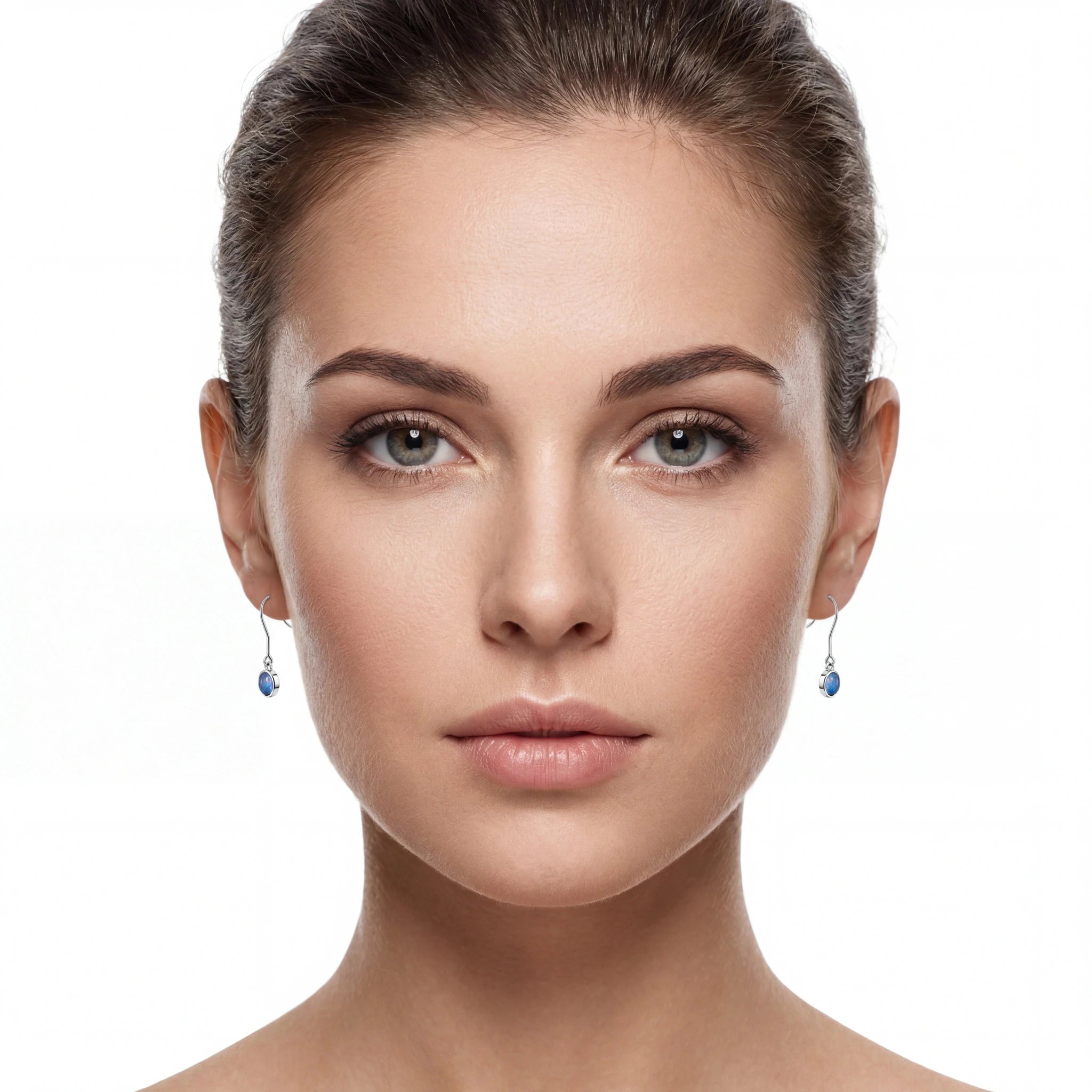 A close-up portrait of a woman with her hair pulled back, wearing small dangling earrings with blue teardrop-shaped stones on silver hooks, against a plain white background.
