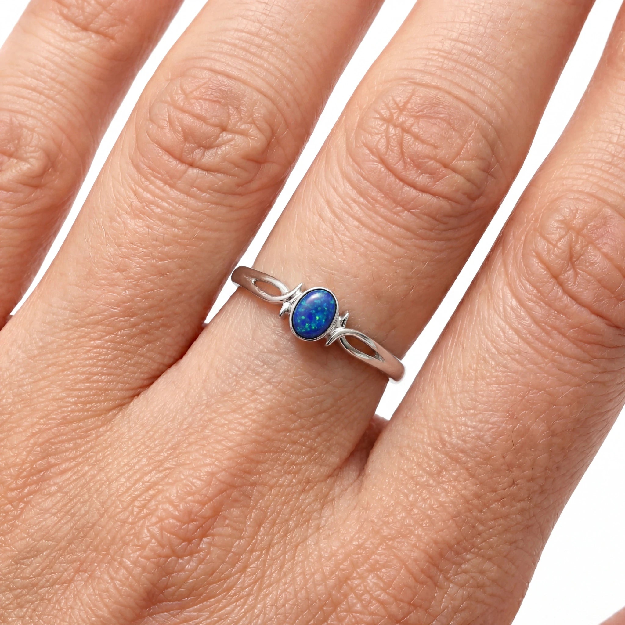 Silver ring with a blue gemstone on a person's finger against a white background