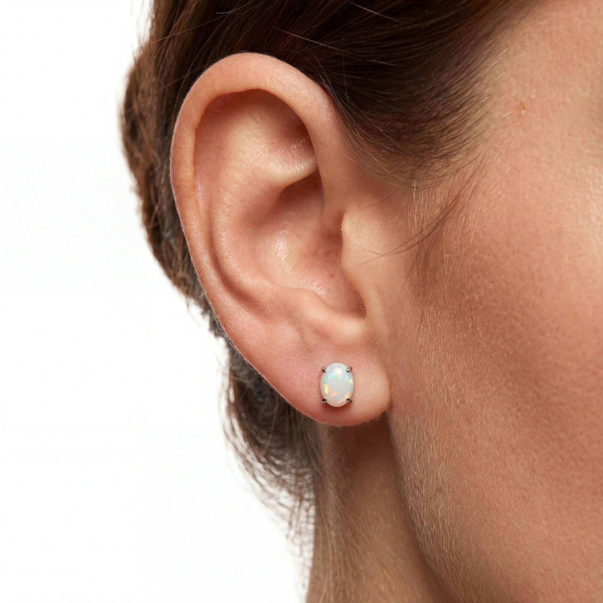 Close-up of an ear wearing a small opal stud earring on a plain background