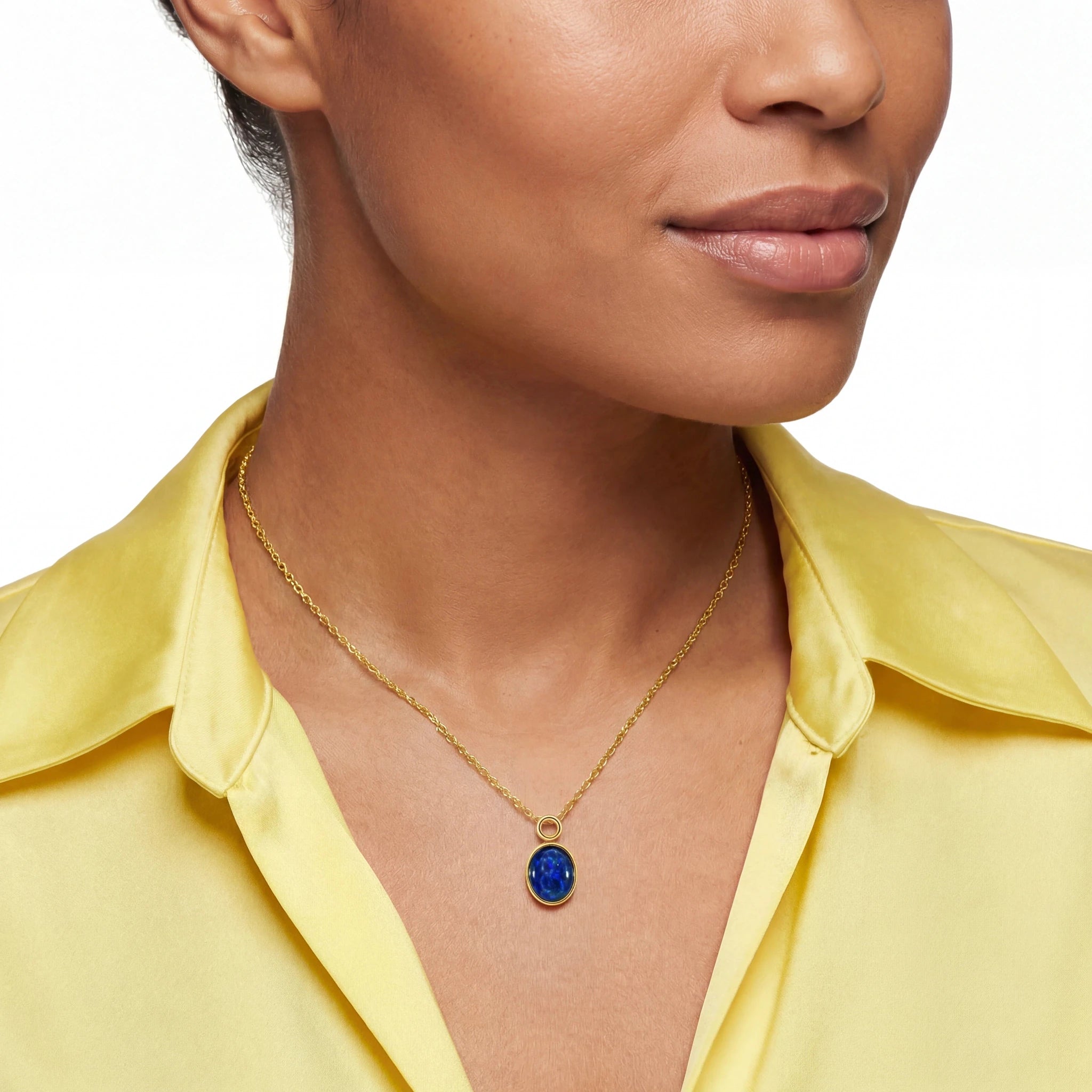 Woman wearing a gold necklace with a blue pendant against a white background