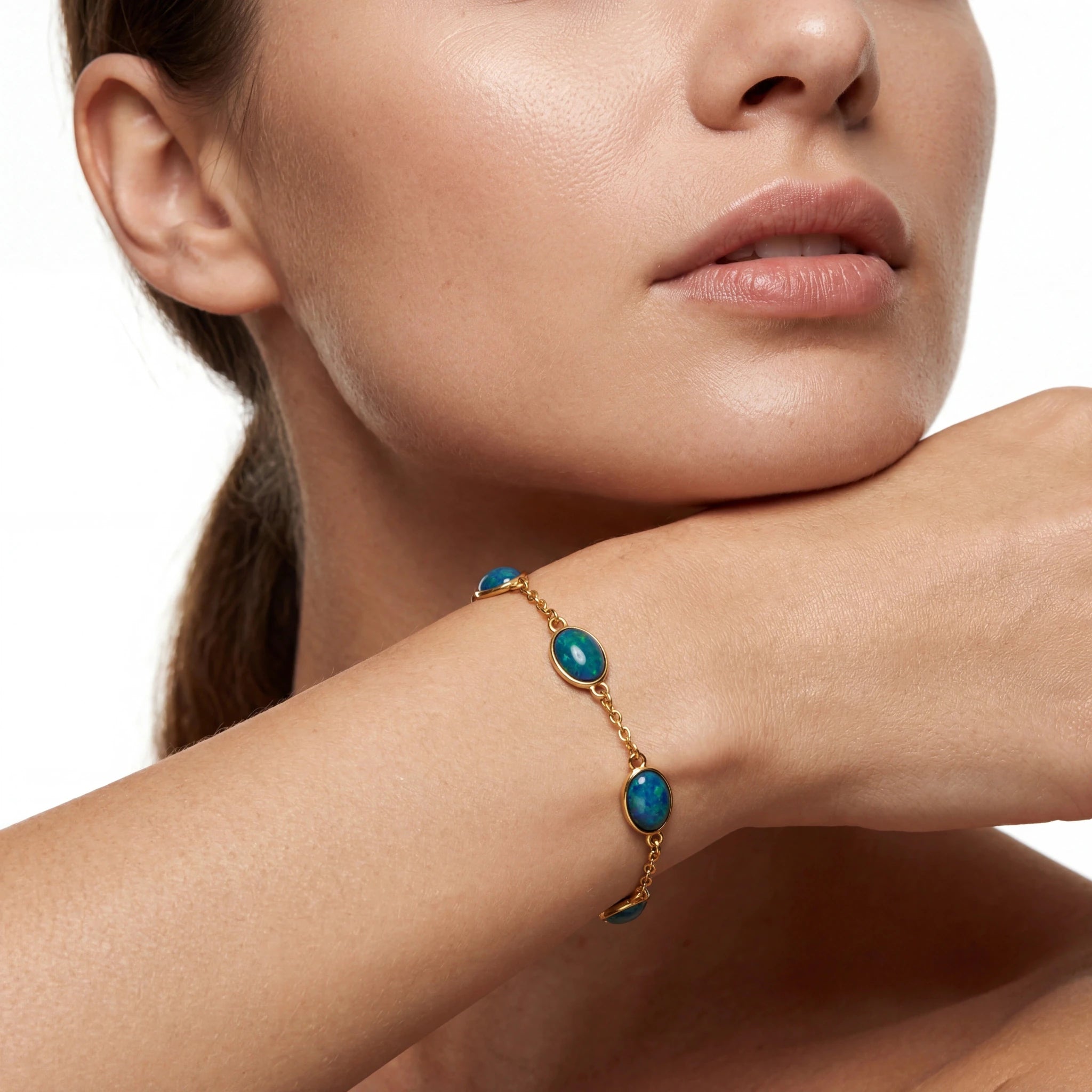 Close-up of a woman's arm wearing a gold bracelet with blue stones on a white background