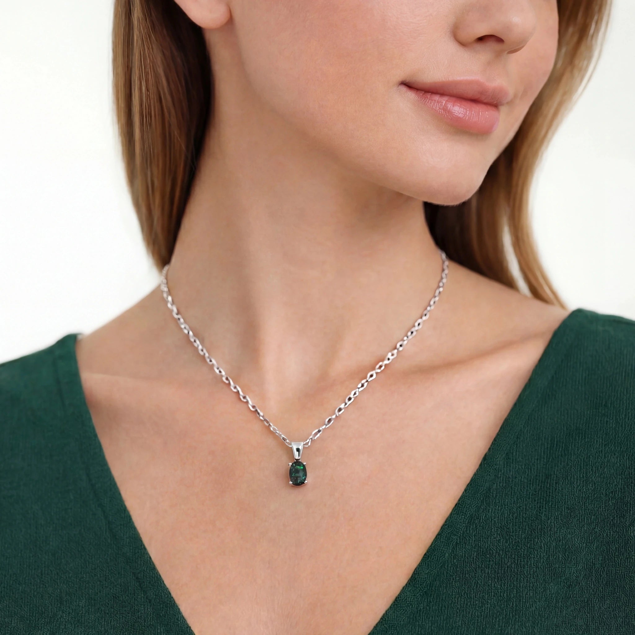 Woman wearing a silver necklace with a green gemstone pendant on a white background