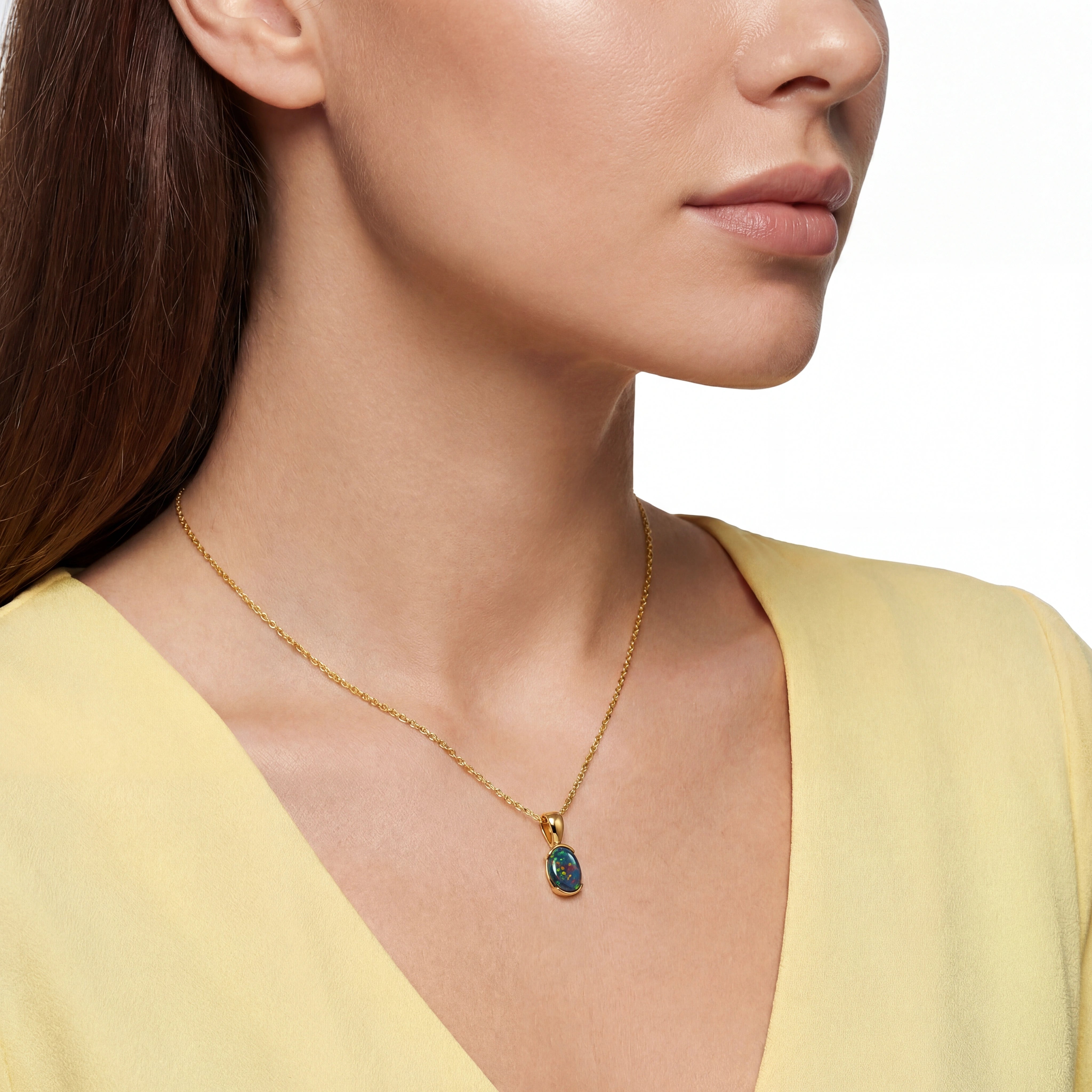 Close-up of a woman wearing a gold necklace with a green pendant on a white background