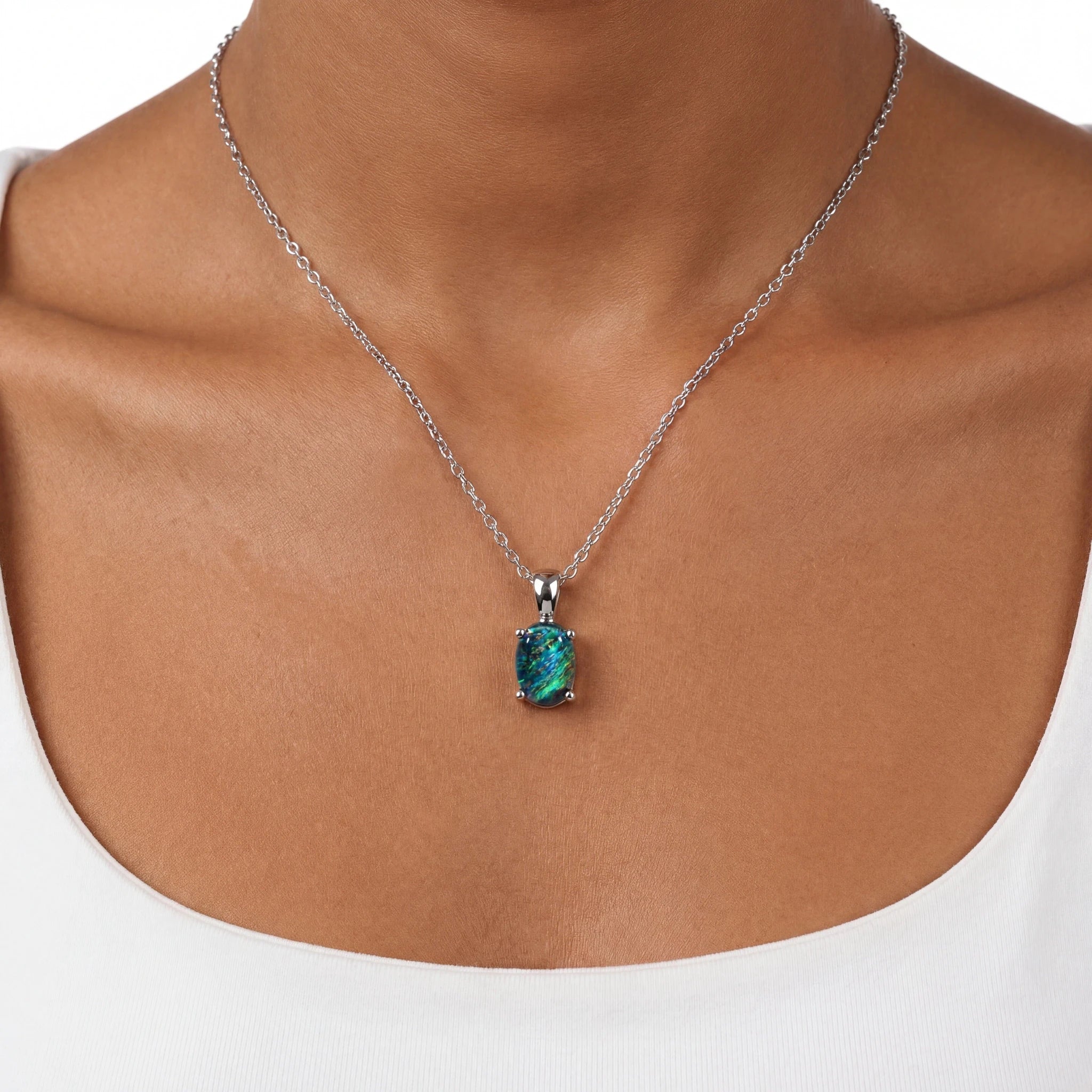 Necklace with a pendant featuring a green gemstone on a person wearing a white top.