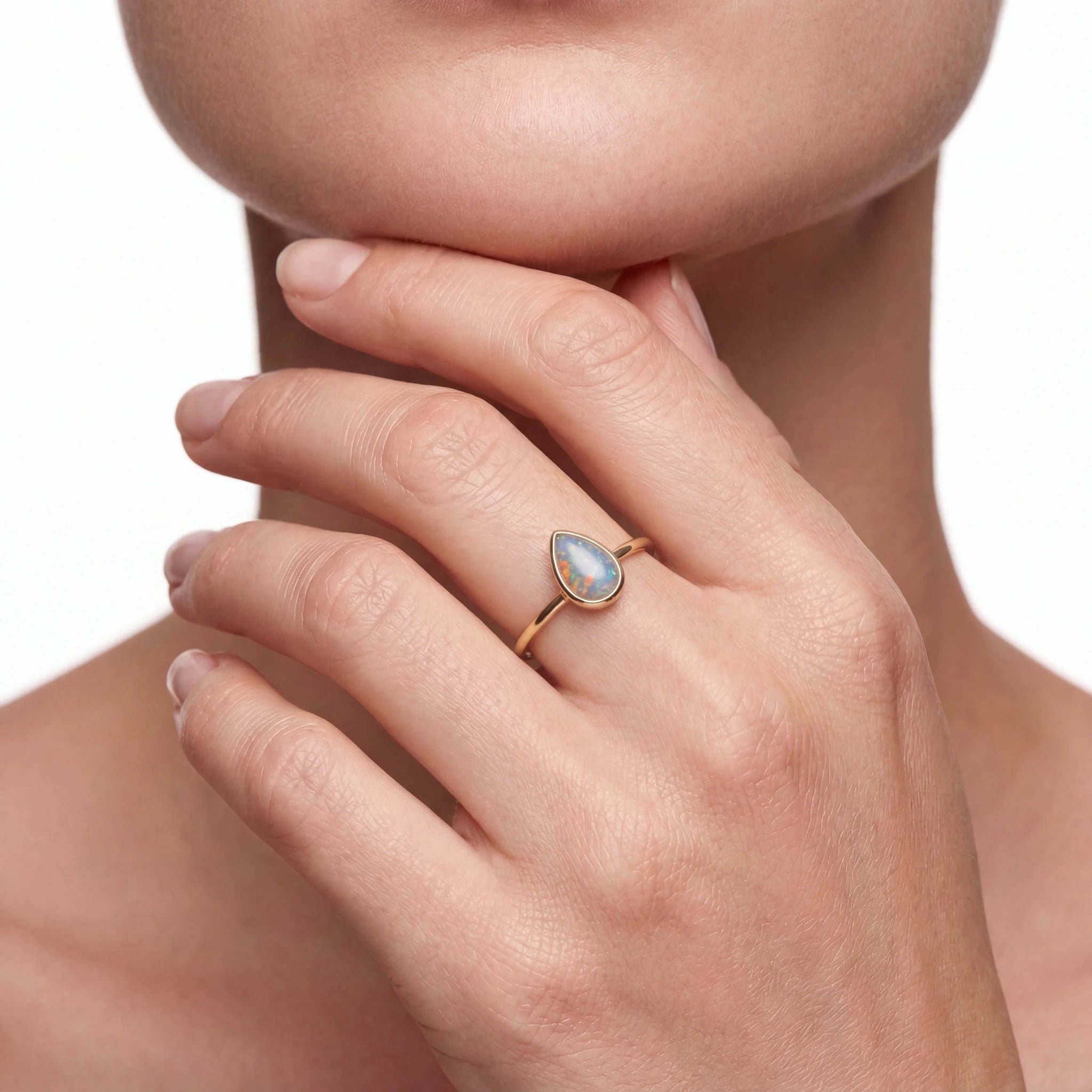 Woman wearing a ring with a teardrop-shaped gemstone on a neutral background