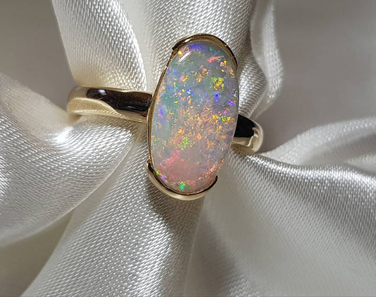 Crystal opal sitting on a cloth. Light is shining onto the opal to display the vibrant colours.