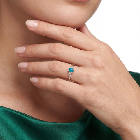 Close-up of a hand wearing a turquoise opal gemstone ring on a neutral background