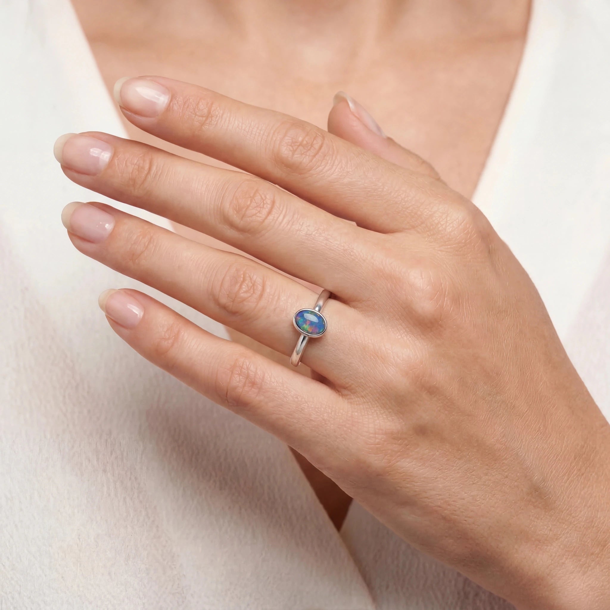 A close-up of a hand wearing a silver ring with an oval blue gemstone, set against a soft white top.