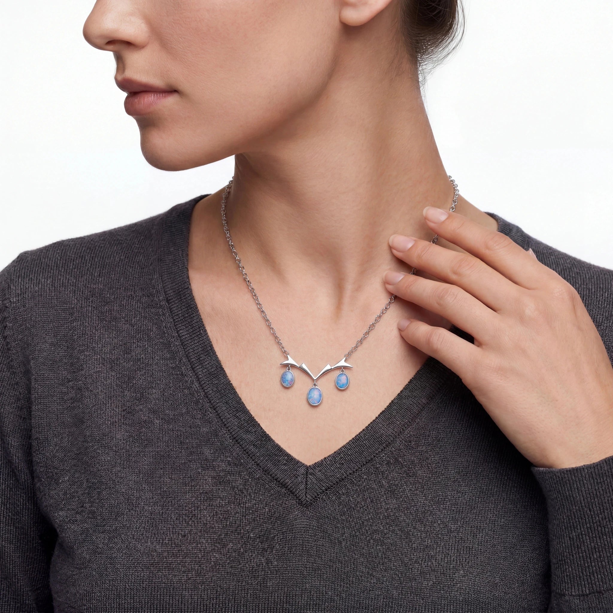 Woman wearing a silver necklace with blue pendant on a plain background