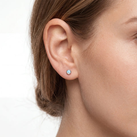 Close-up of a woman wearing a small round earring with a light opal gemstone 