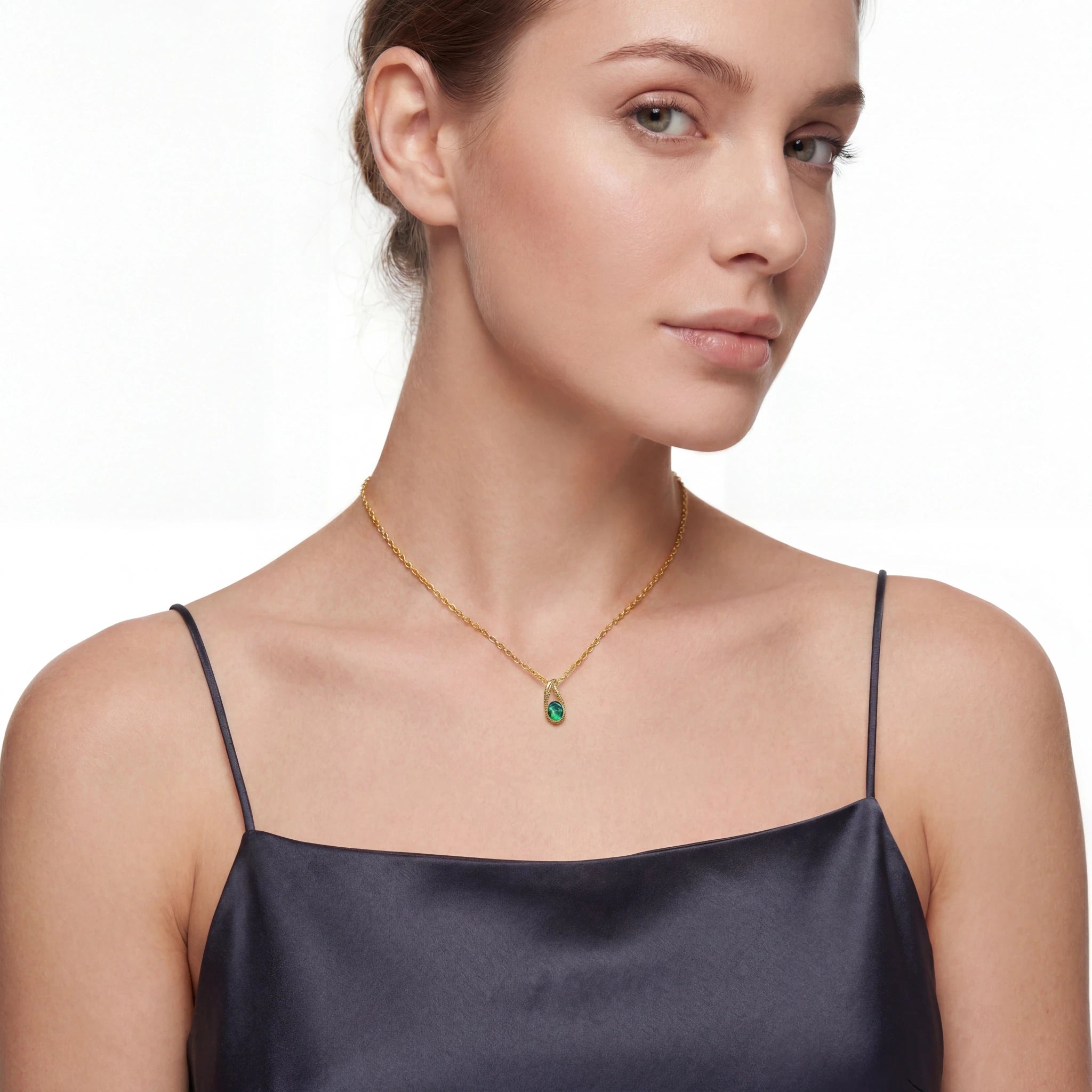 Woman wearing a gold necklace with a green pendant on a white background