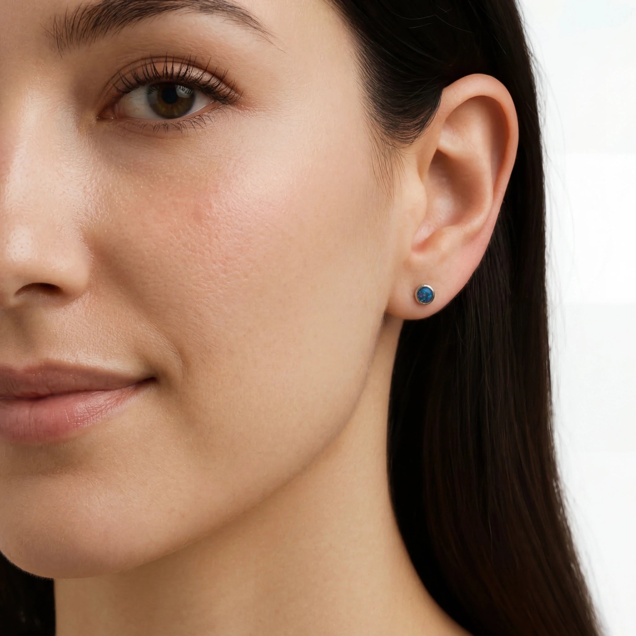 Close-up of a woman wearing a blue opal earring on a white background