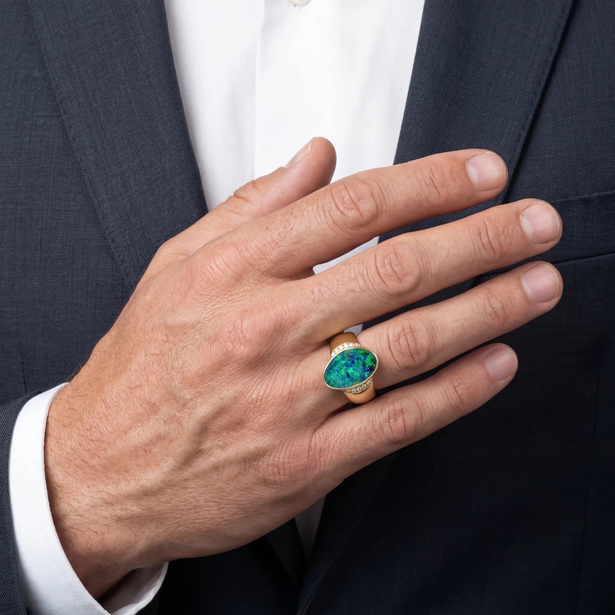 Man wearing a green opal ring with a dark suit background