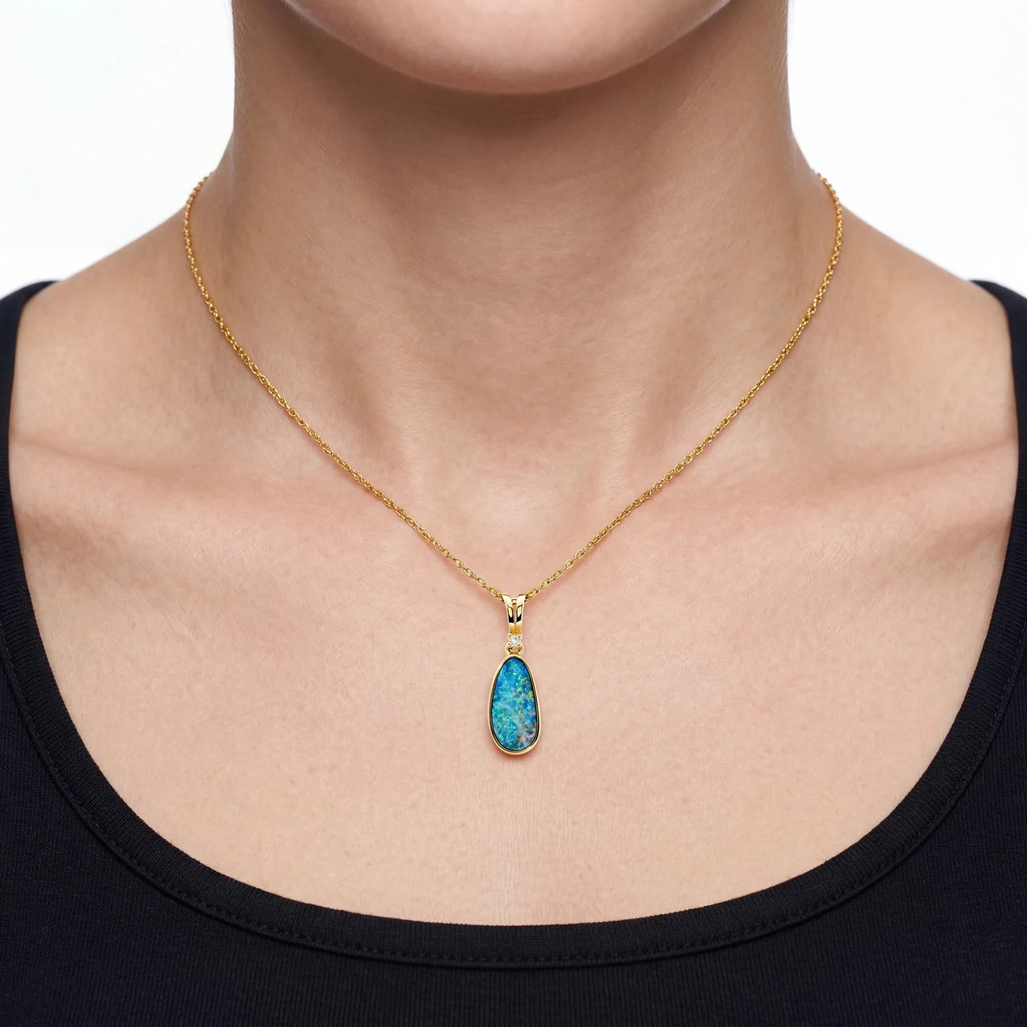 Gold necklace with a blue opal  pendant worn by a person on a white background