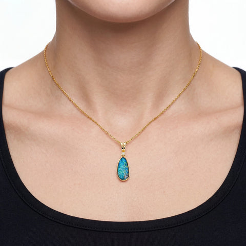 Gold necklace with a blue opal  pendant worn by a person on a white background