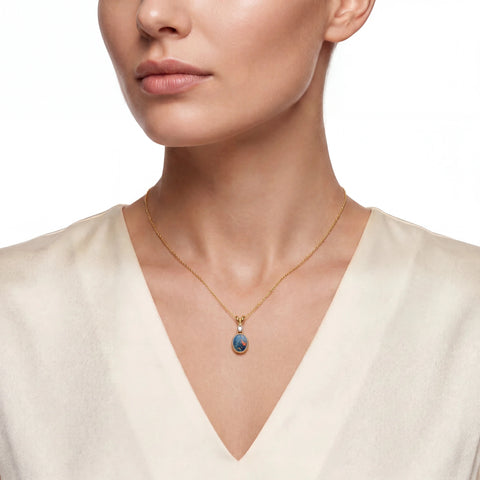 Woman wearing a gold necklace with a blue opal pendant on a white background