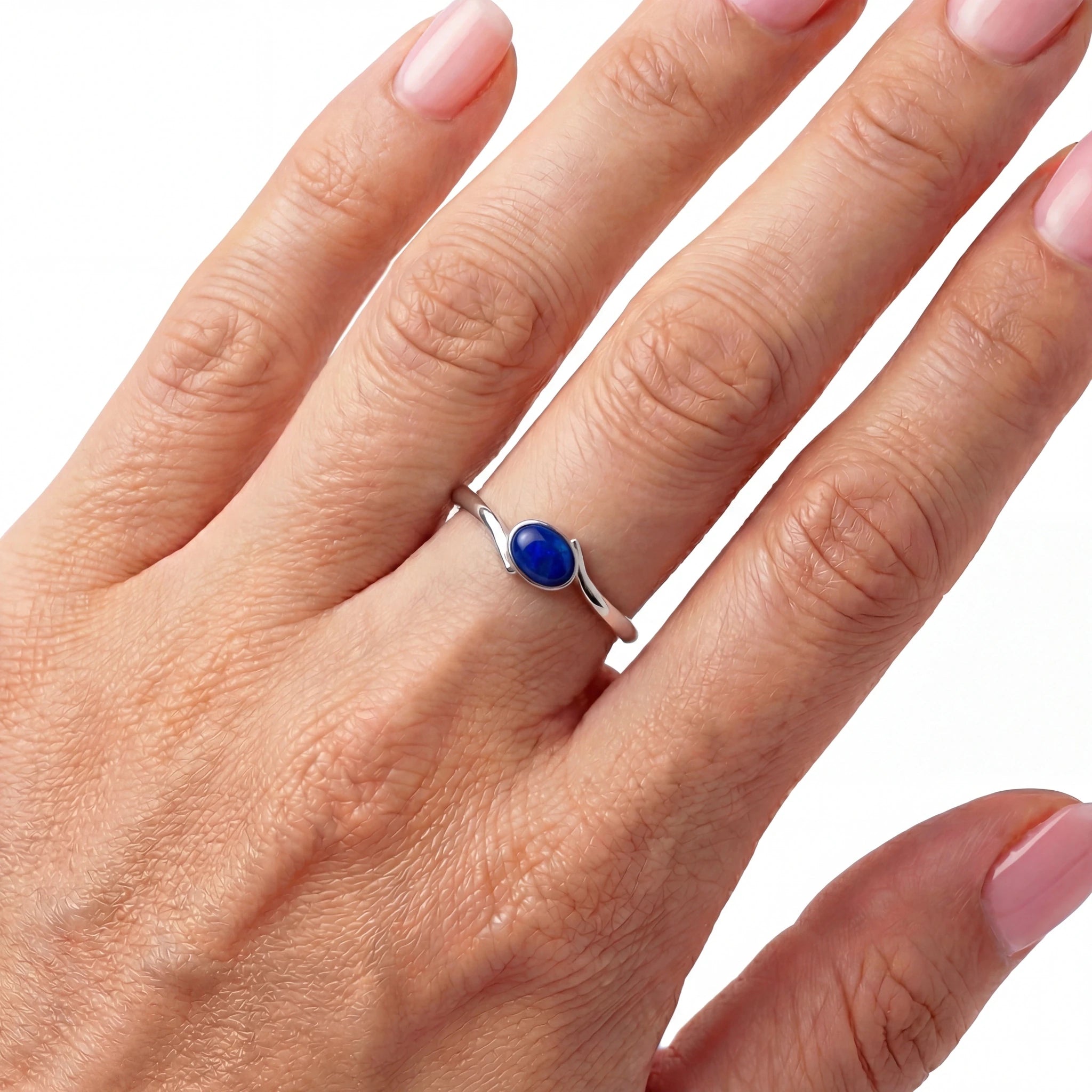 Hand wearing a silver ring with a blue stone on a white background