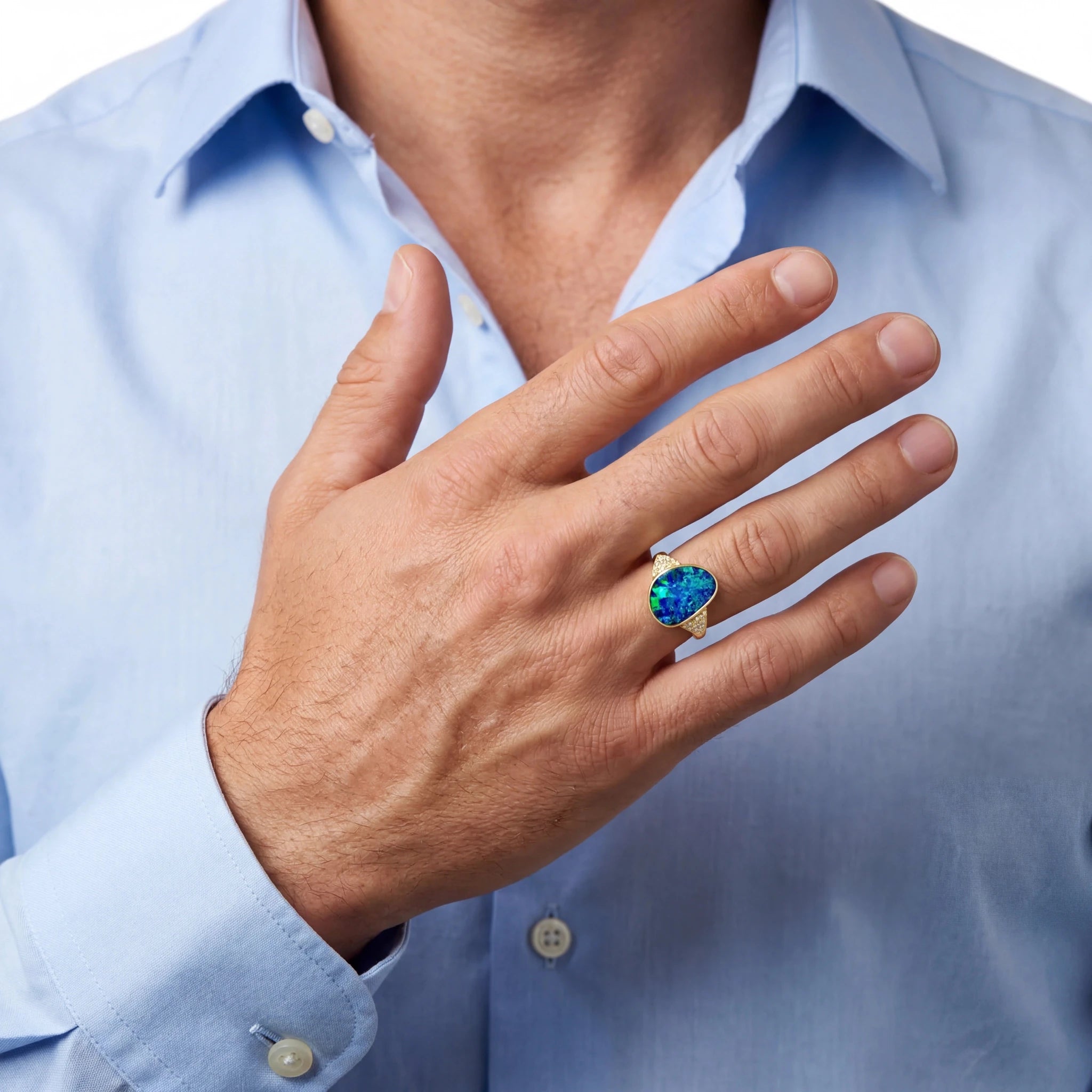 Man wearing a ring with a blue opal gemstone against a light blue shirt background