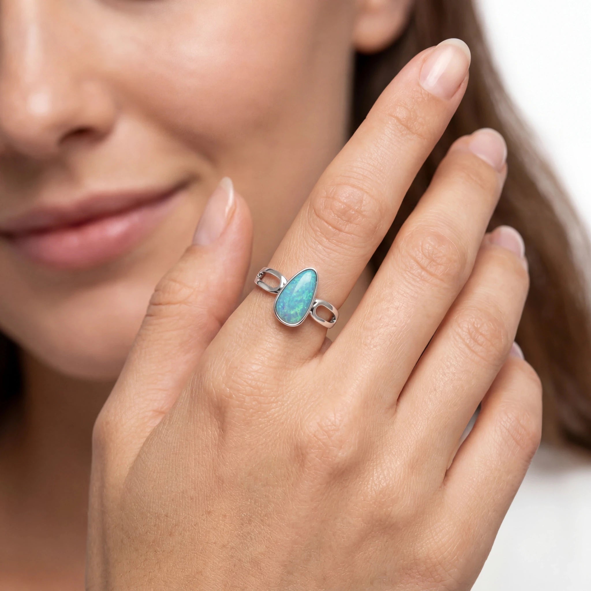 Close-up of a hand wearing a silver ring with a blue gemstone on a neutral background