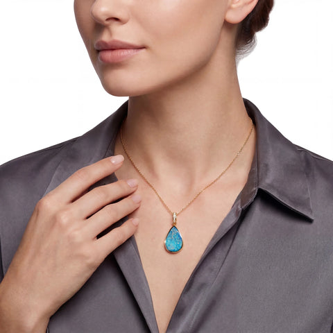 Woman wearing a gold necklace with a blue teardrop opal pendant on a white background