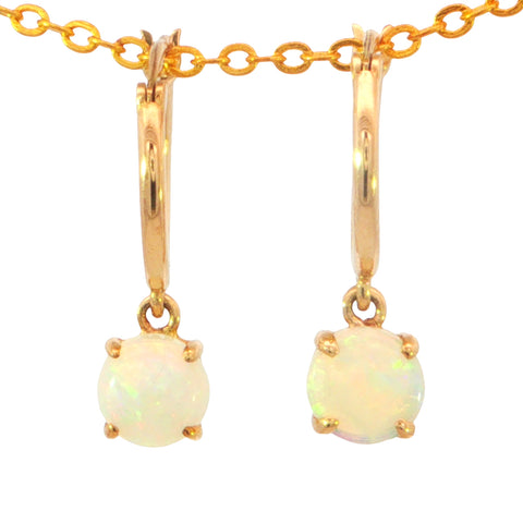 A pair of gold huggie hoop earrings with round white opal gemstones, suspended from a gold chain on a plain white background.