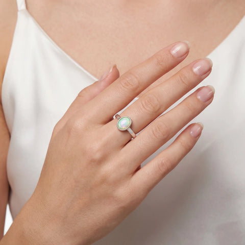 Woman wearing a ring with a green gemstone on a neutral background