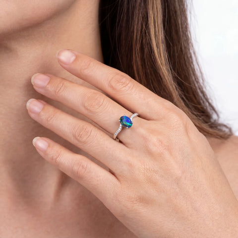 Close-up of a hand wearing a ring with a colourful gemstone on a neutral background