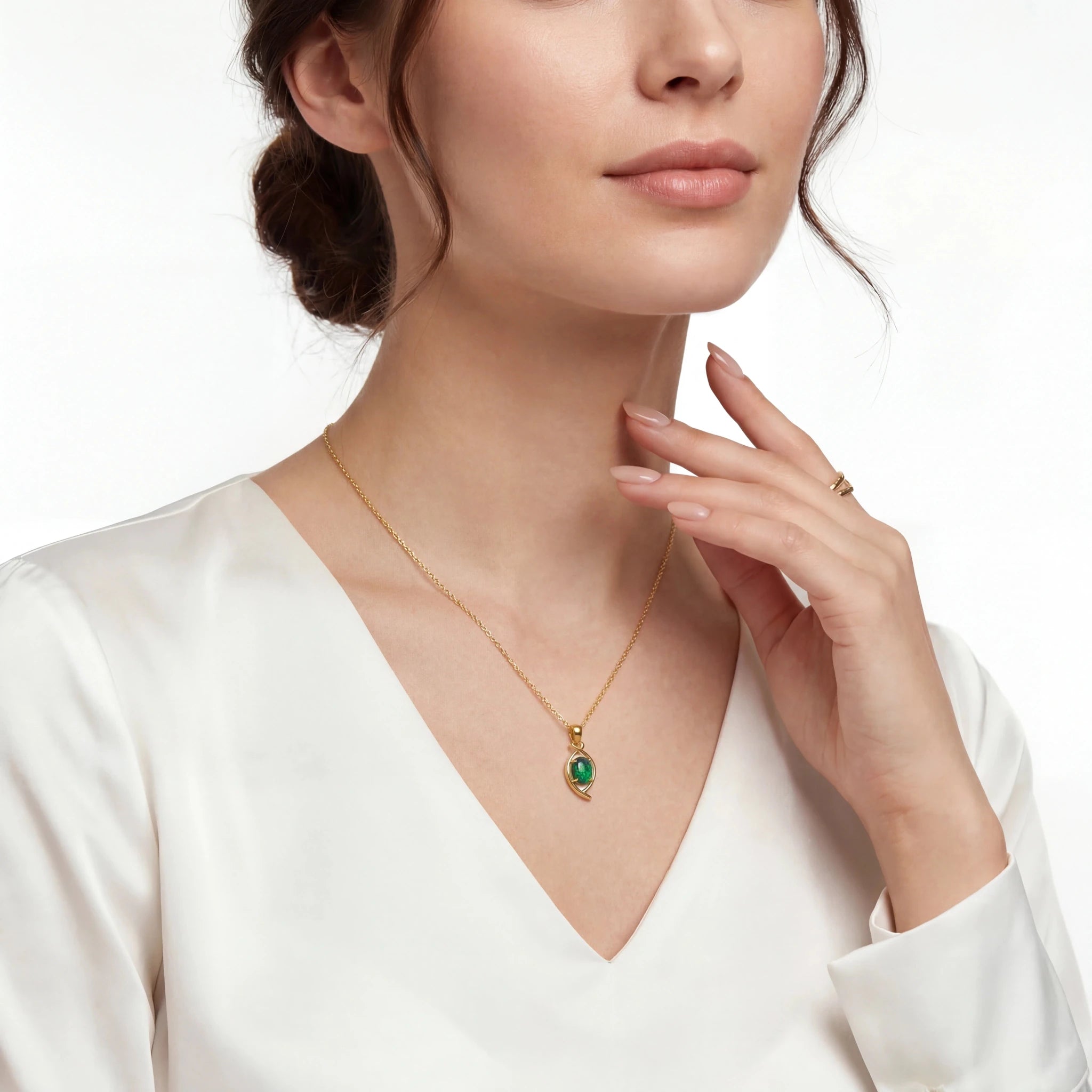 Woman wearing a gold necklace with a green pendant on a white background