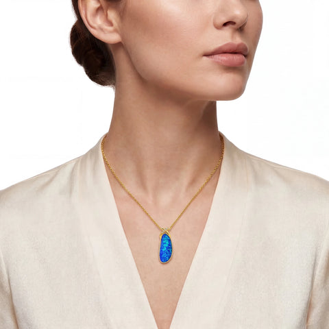 Woman wearing a gold necklace with a blue opal pendant on a white background