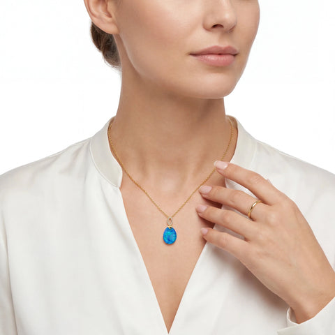 Woman wearing a gold necklace with a blue opal pendant and a ring on a white background