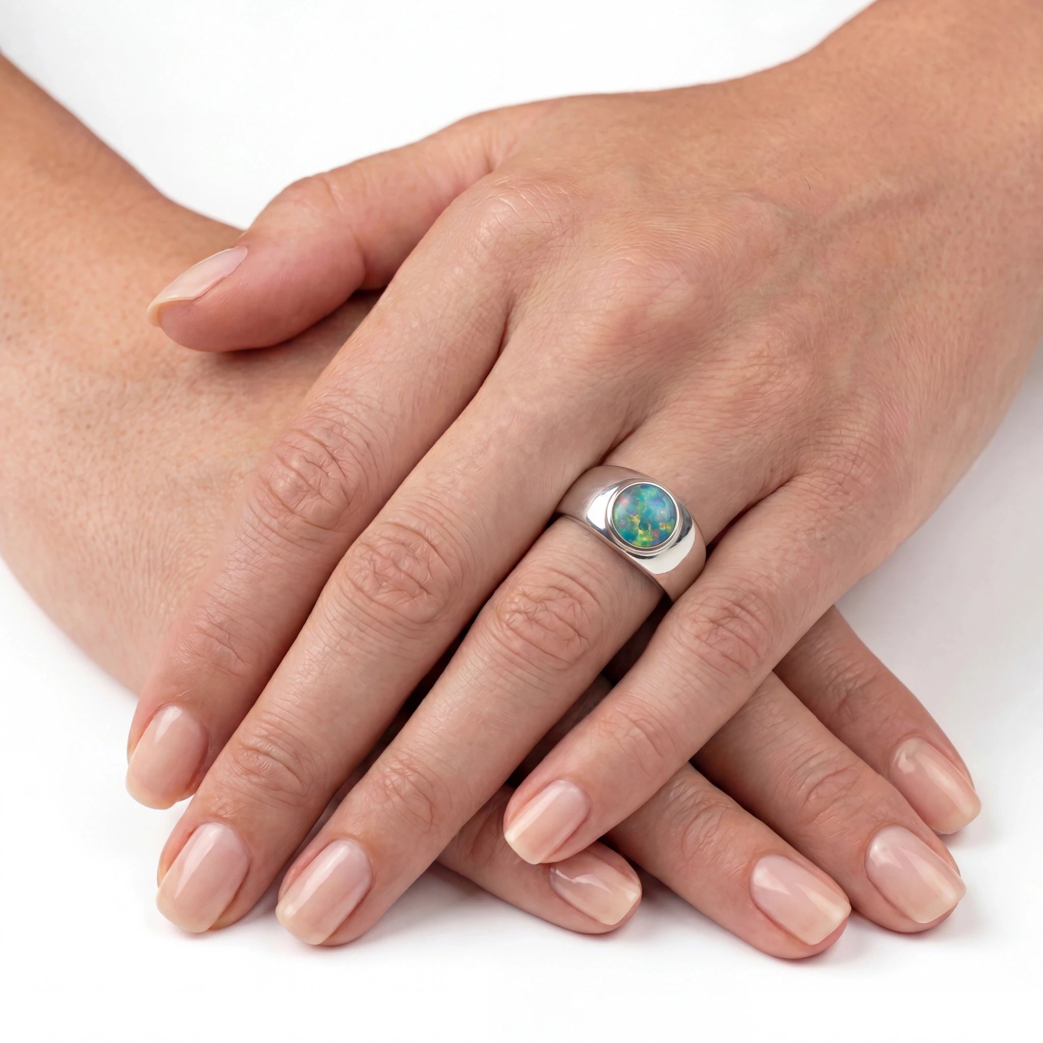 Close-up of a hand wearing a silver ring with an opal stone on a white background