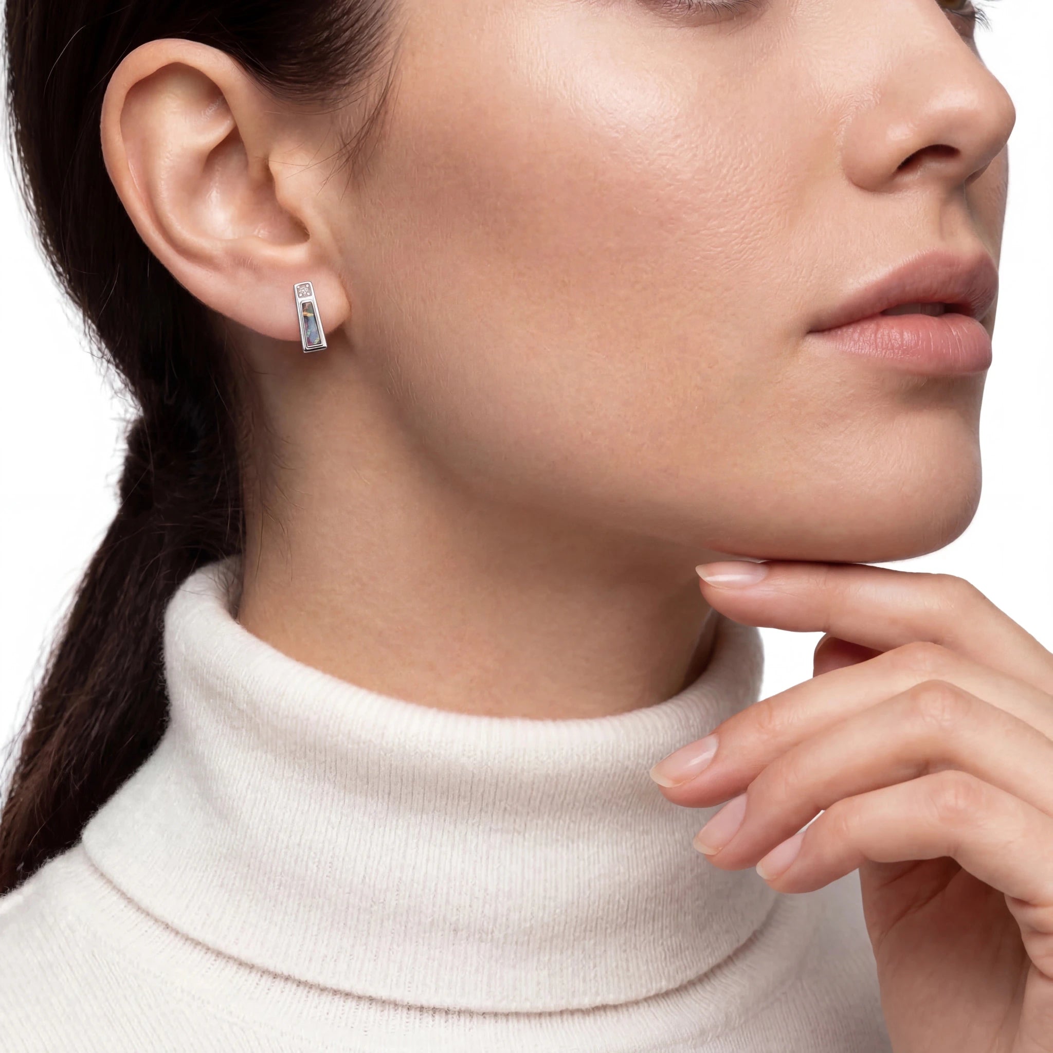 Close-up of a woman wearing a silver opal earring with a white turtleneck sweater.