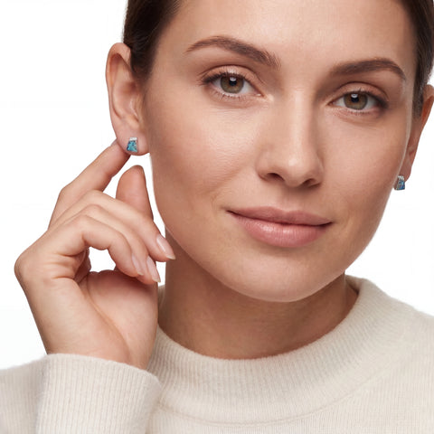 Close-up of a woman wearing opal earrings with a plain background