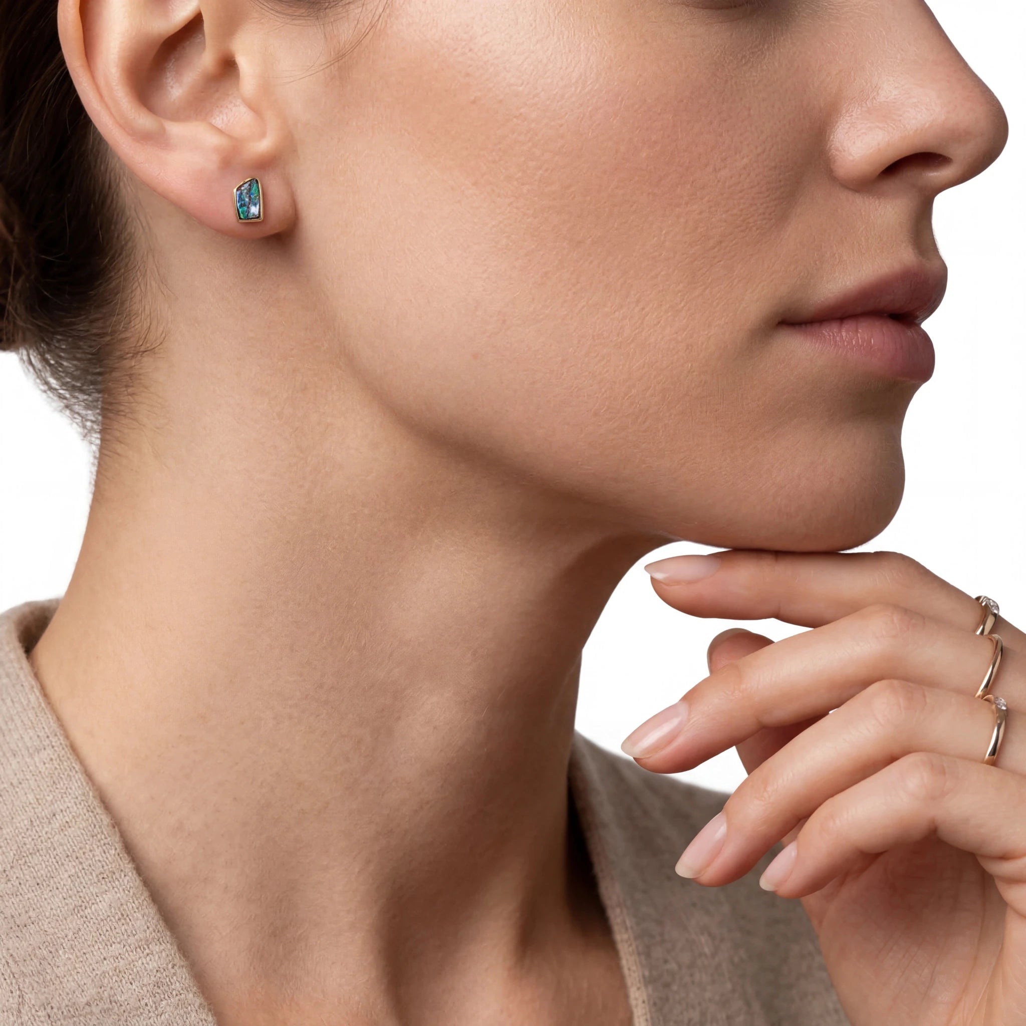 Close-up of a woman wearing earrings and rings with a neutral background