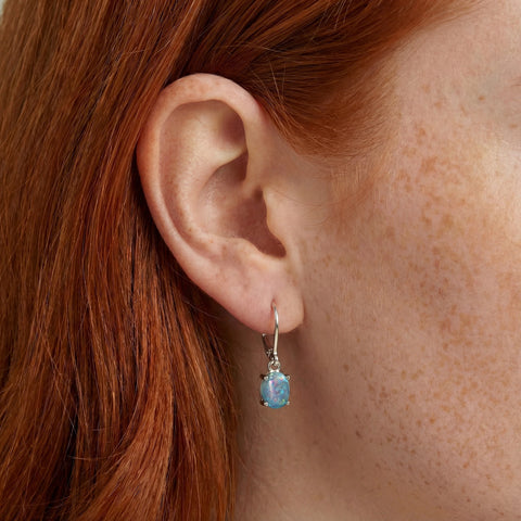 Close-up of an ear wearing a blue gemstone earring with red hair.
