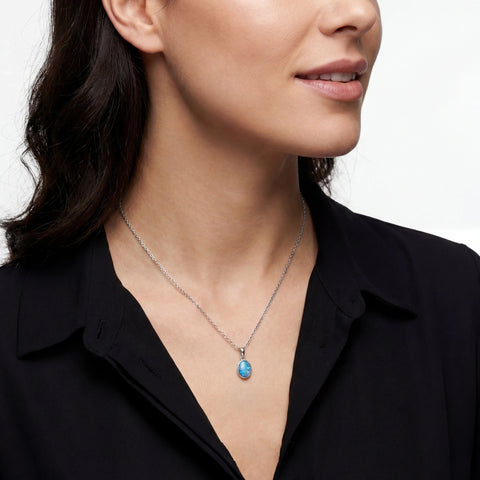 Woman wearing a necklace with a blue pendant against a neutral background