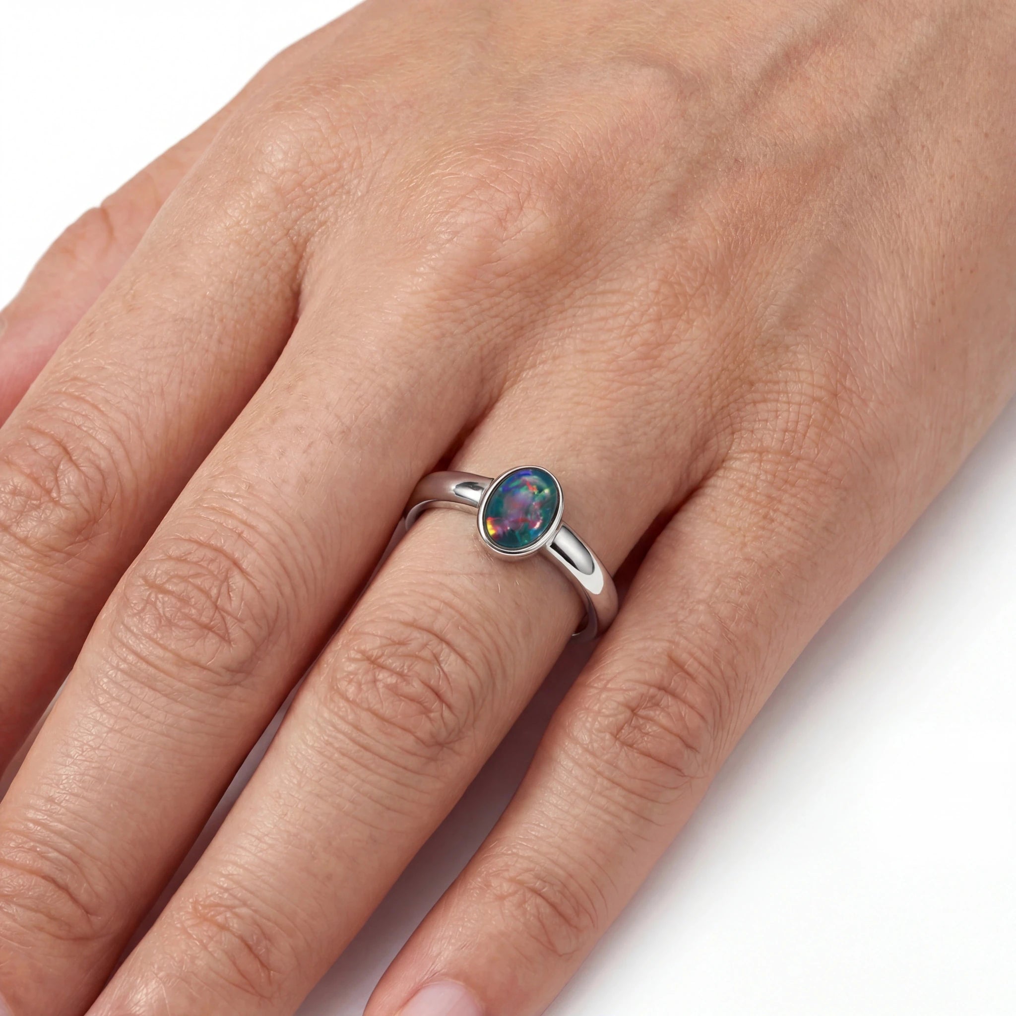 A silver ring with an oval iridescent opal gemstone worn on a person's finger, shown against a clean white background.