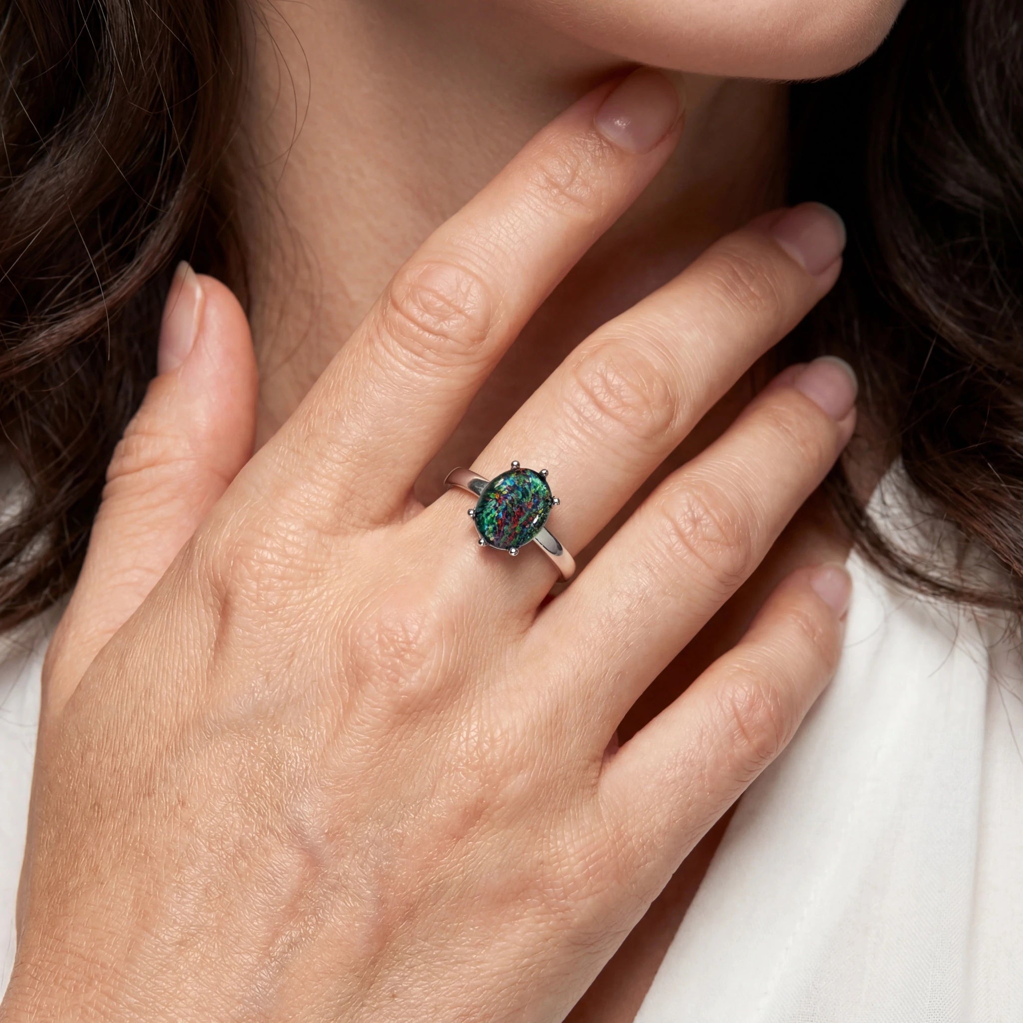 Close-up of a hand wearing a ring with a green gemstone, against a neutral background.