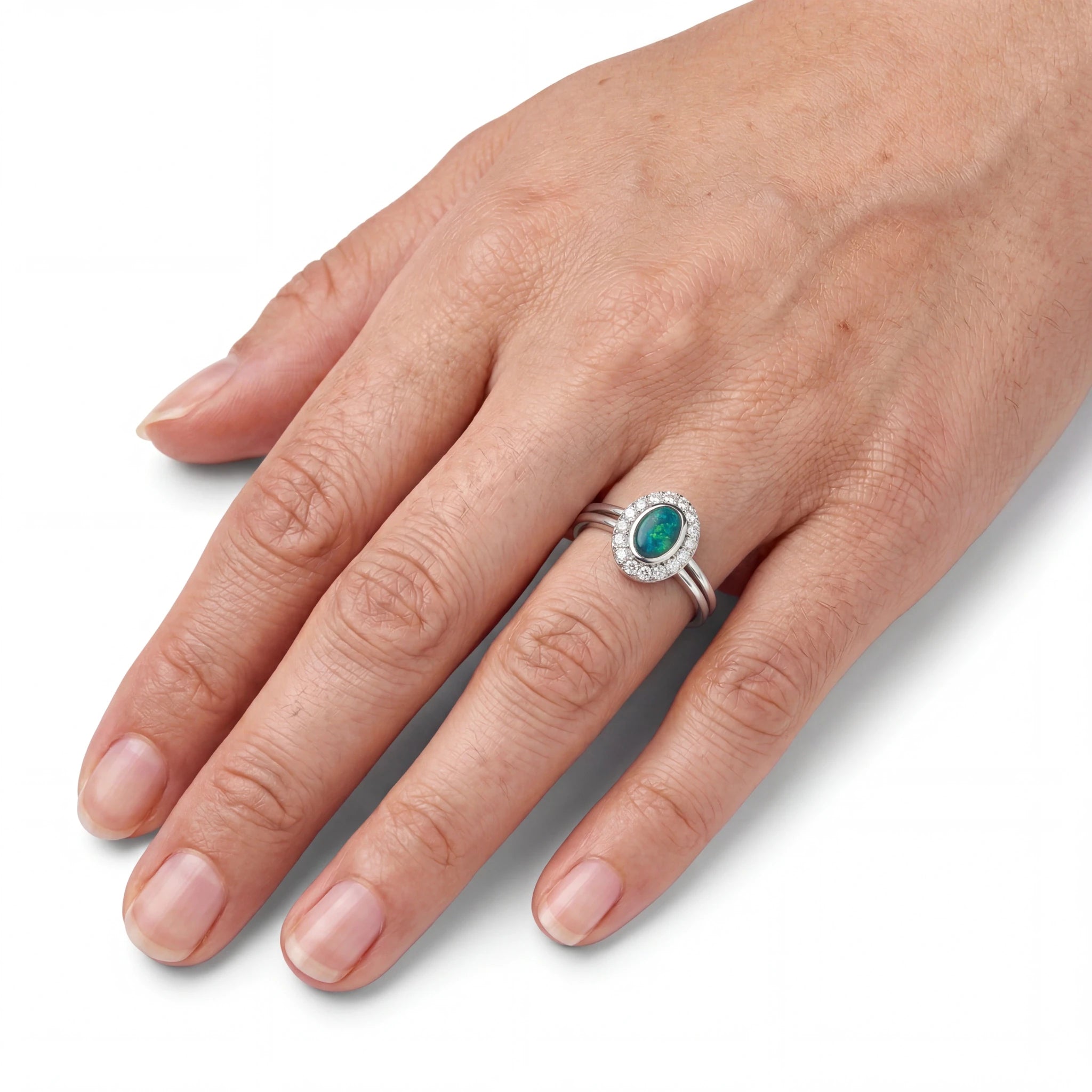 Hand wearing a silver ring with a green gemstone on a white background