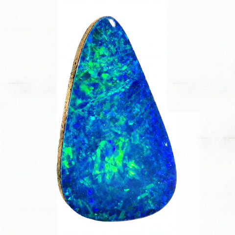A teardrop-shaped cabochon gemstone with a dark blue and black base, displaying vibrant green and blue flashes of opalescent colour, isolated on a white background.