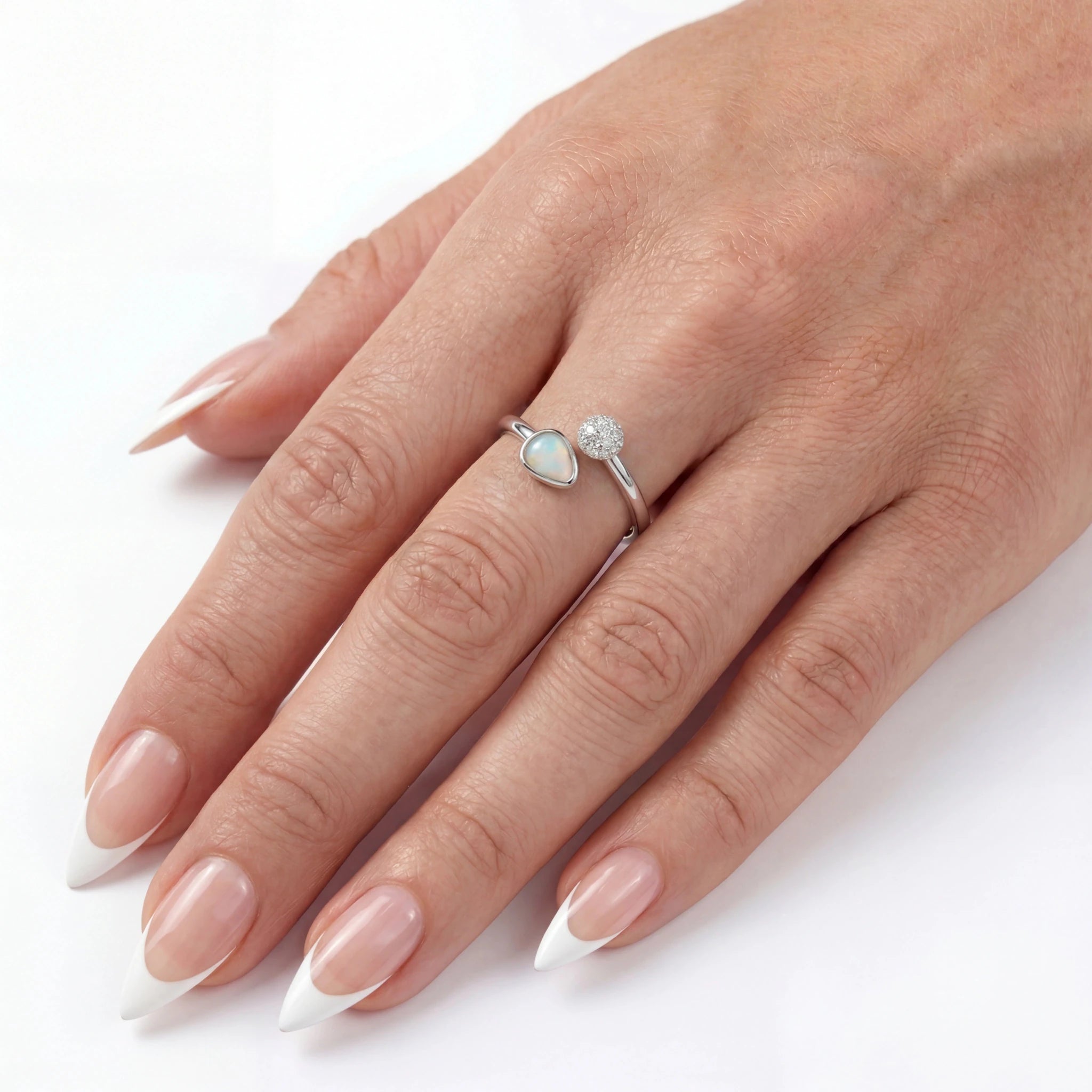 Hand wearing a silver ring with a heart-shaped gemstone on a white background