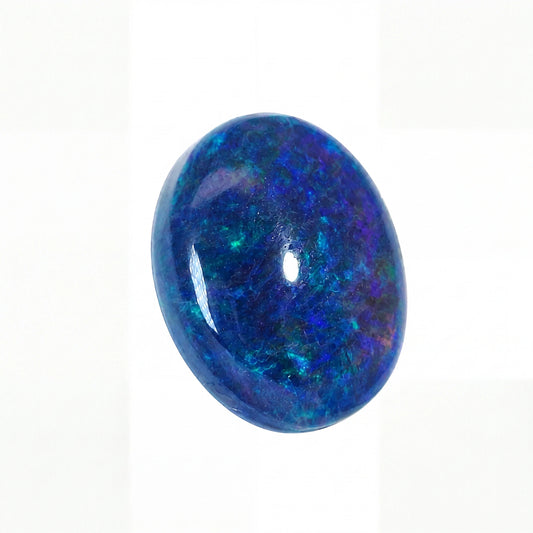 A polished oval cabochon gemstone featuring vibrant blue and green iridescent opal patterns, set against a plain white background.