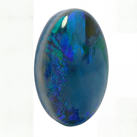 A polished oval cabochon gemstone featuring a deep blue base with vibrant iridescent flashes of green, teal, and purple, set against a plain white background.