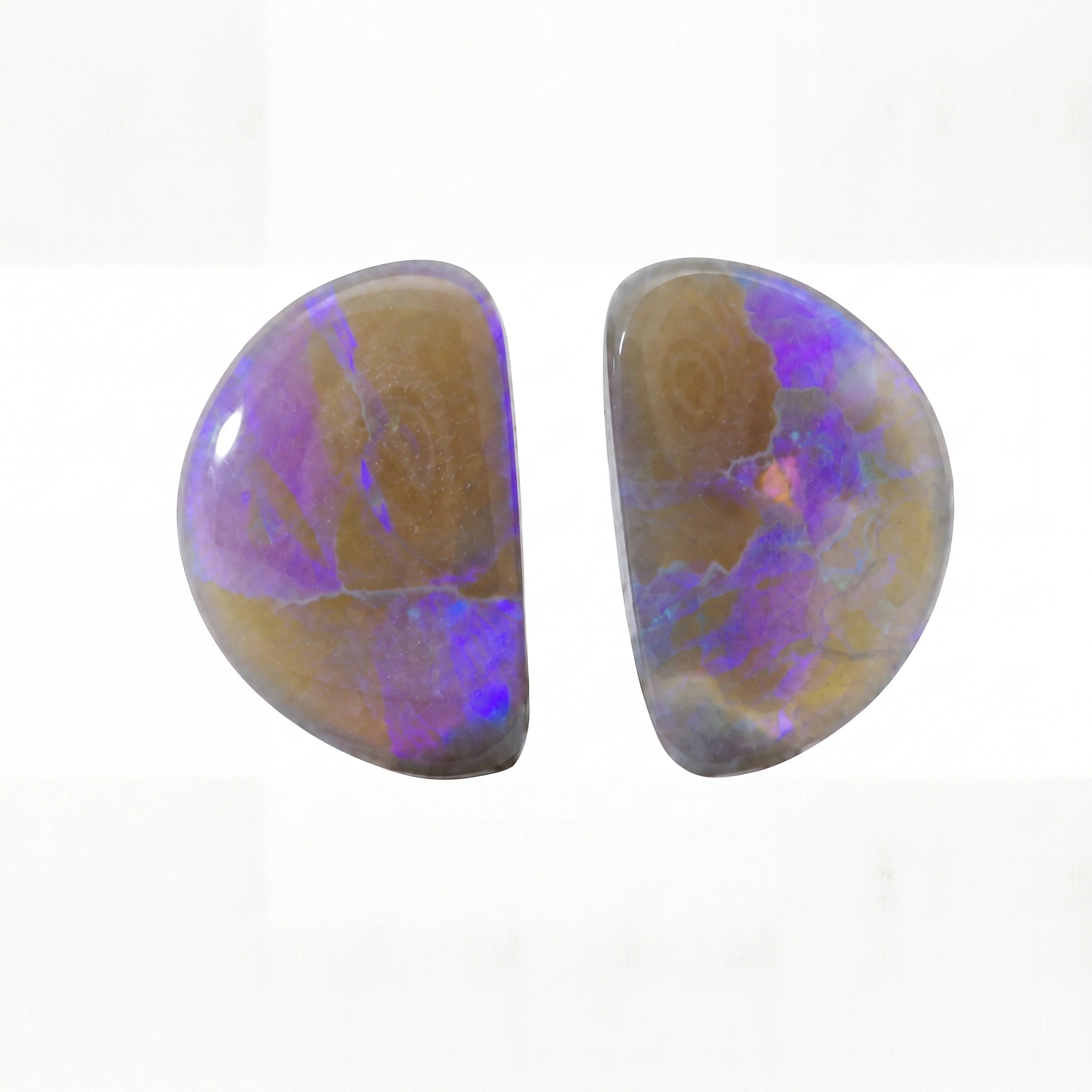 Two polished oval cabochon gemstones showing a mix of brown, purple, and blue iridescent opal patterns on a white background.