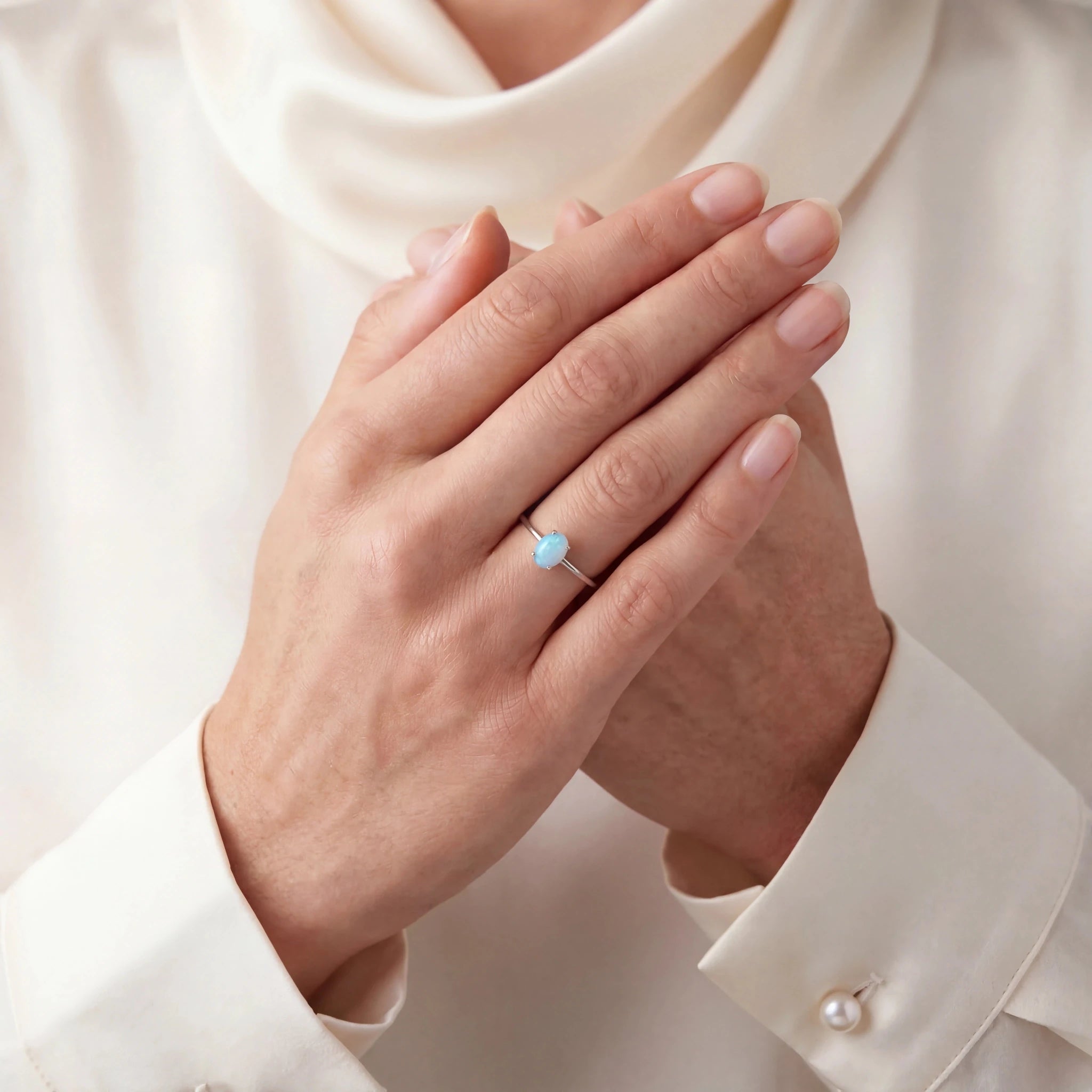Close-up of hands with a ring featuring a blue gemstone, wearing a white shirt.