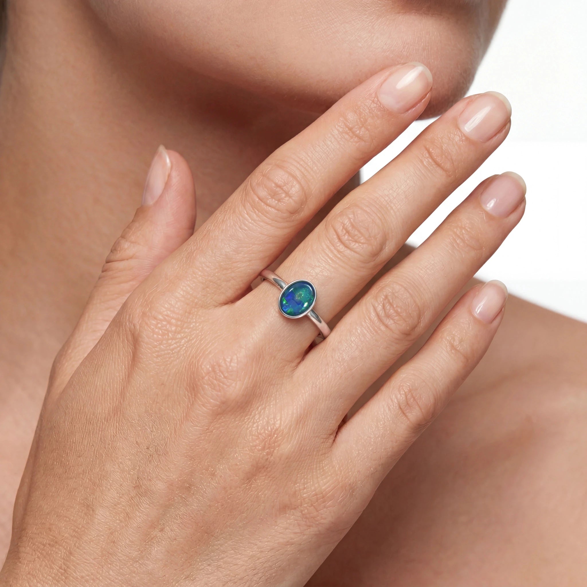 Close-up of a hand wearing a silver ring with a green gemstone on a neutral background