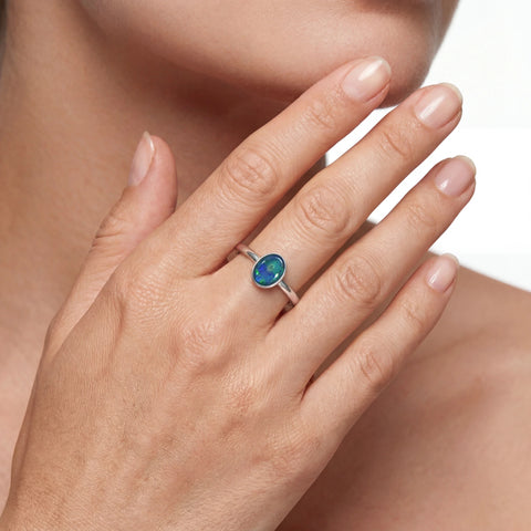 Close-up of a hand wearing a silver ring with a green gemstone on a neutral background